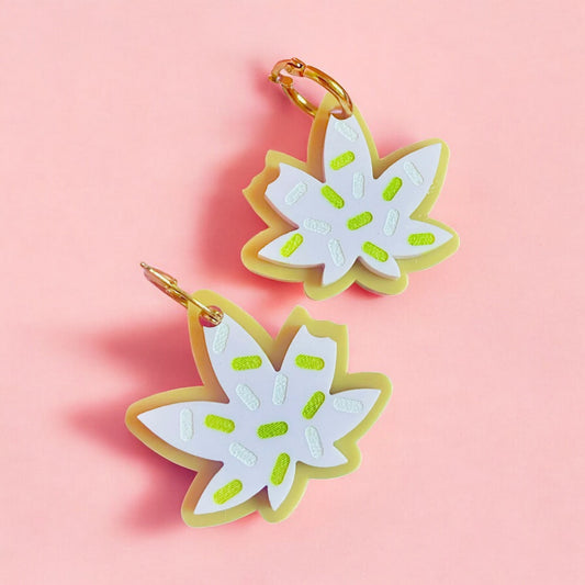 a pair of earrings in the shape of a pot leaf cookie with a bite taken out with white icing with green and white sprinkles.  perfect gift for the 420 lover.