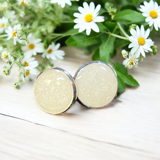 Pair of round beige earrings with silver accents on a wooden surface with daisies in the background