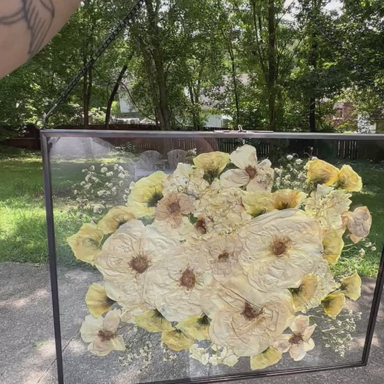 A custom pressed flower floating frame with white roses , and green eucalyptus .   A beautiful way to preserve a bridal bouquet.