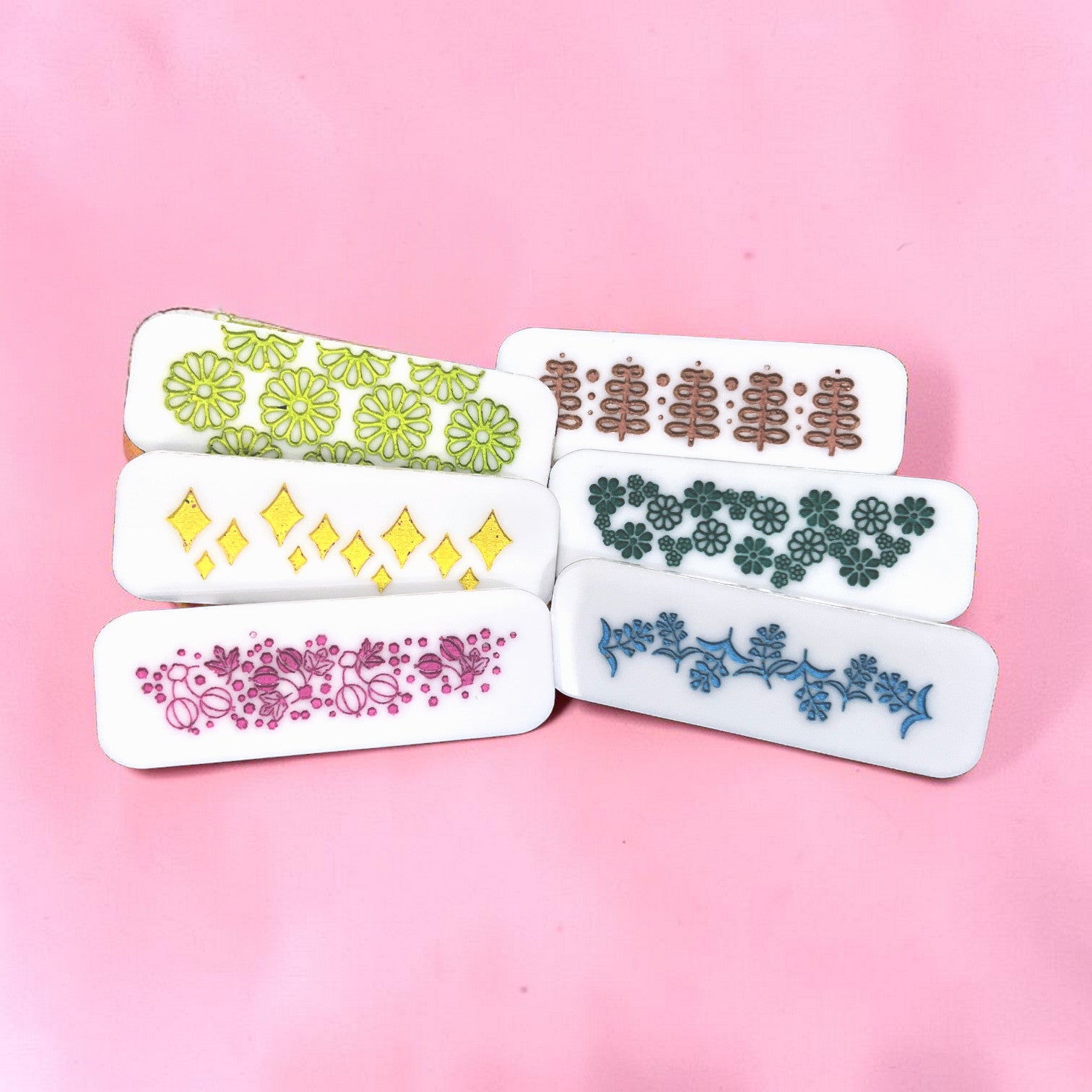 Five small rectangular hair clips with floral patterns on a pink background