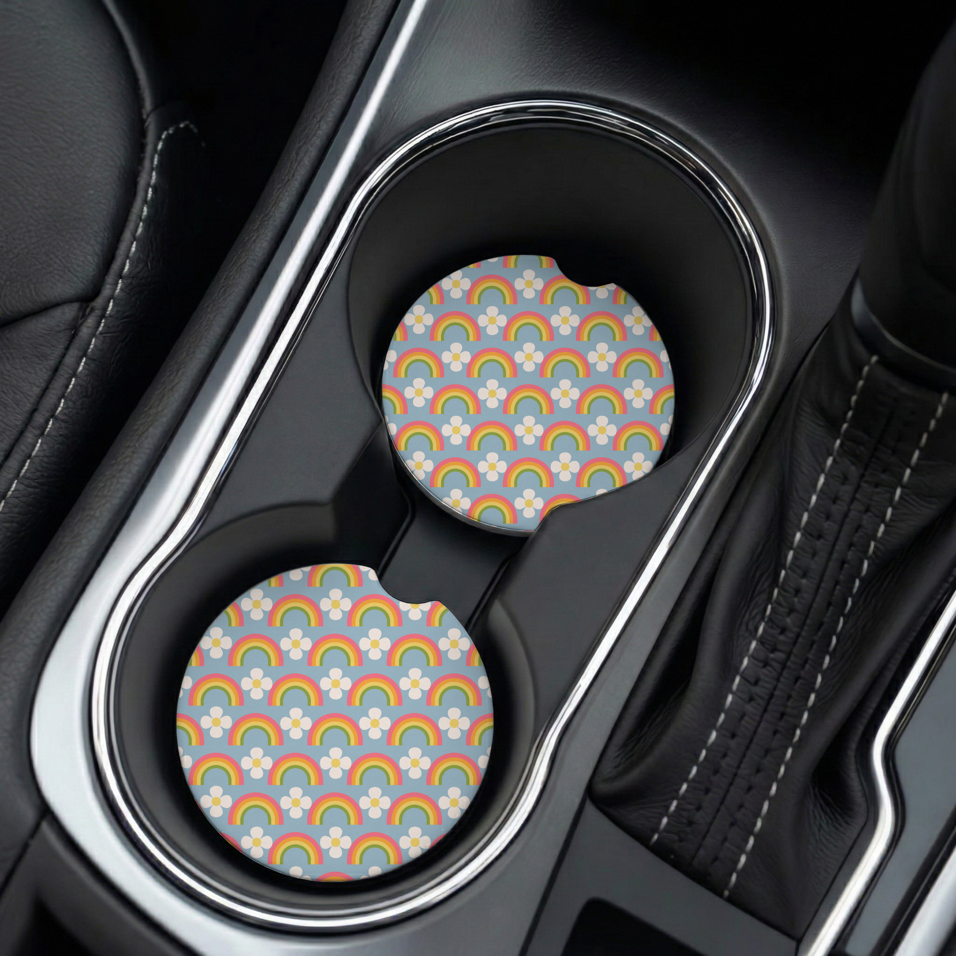 Car cup holder with two colorful patterned coasters on a black leather interior.