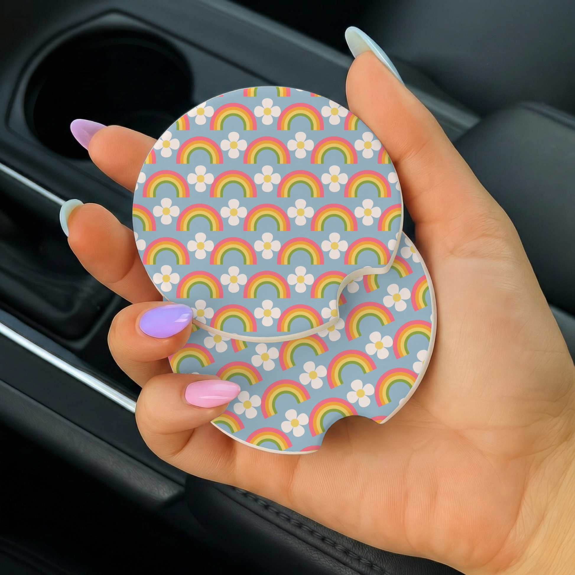 Hand holding a car coaster with rainbow and flower pattern