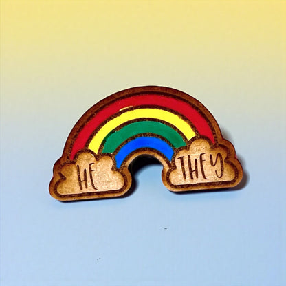 Rainbow-shaped pin with 'HE' and 'THEY' on clouds against a gradient background