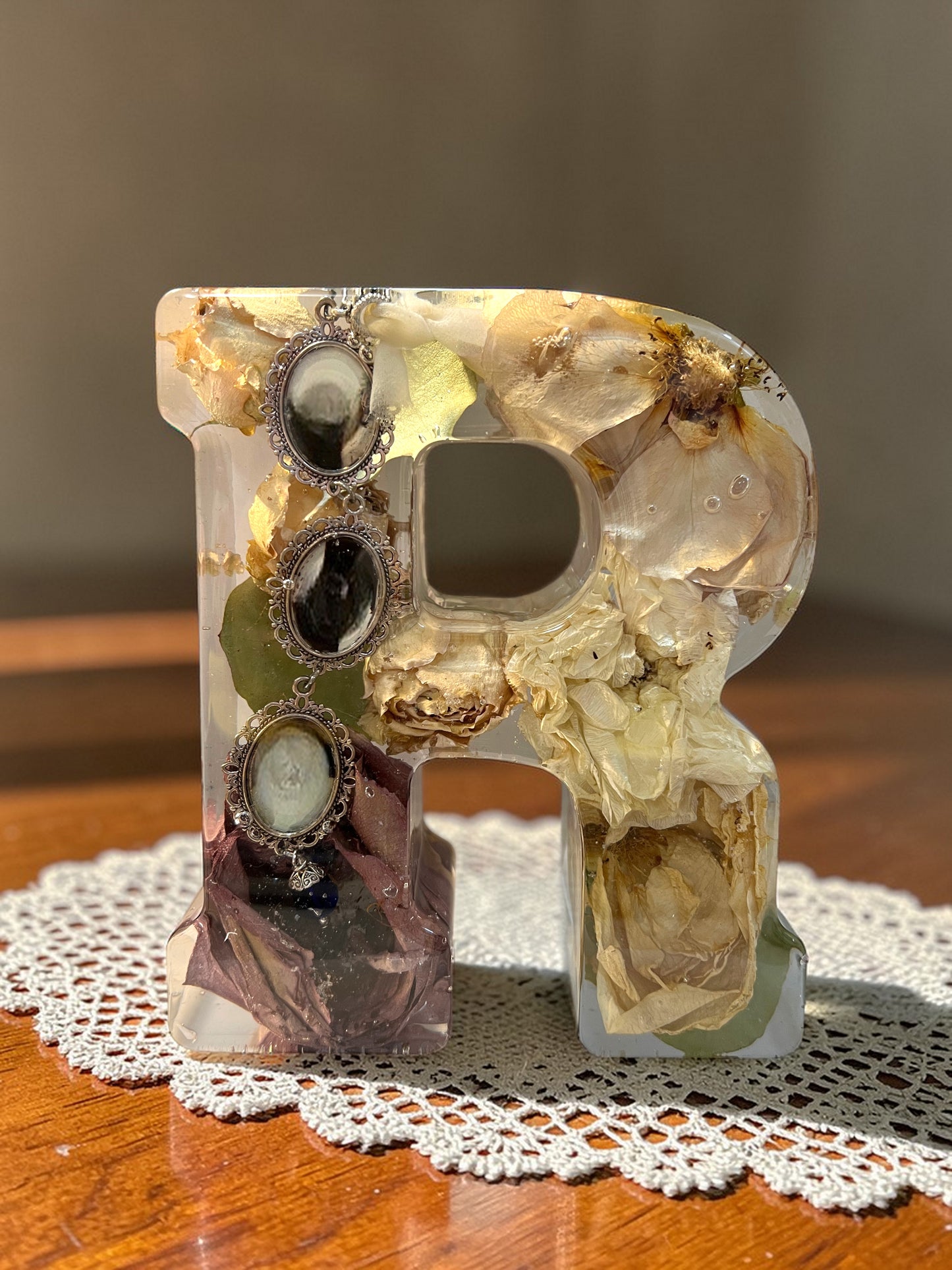 Decorative letter 'r' with embedded jewelry on a wooden surface