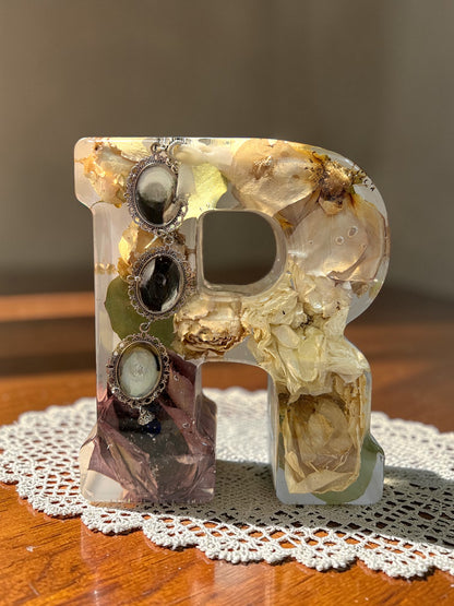 Decorative letter 'r' with embedded jewelry on a wooden surface