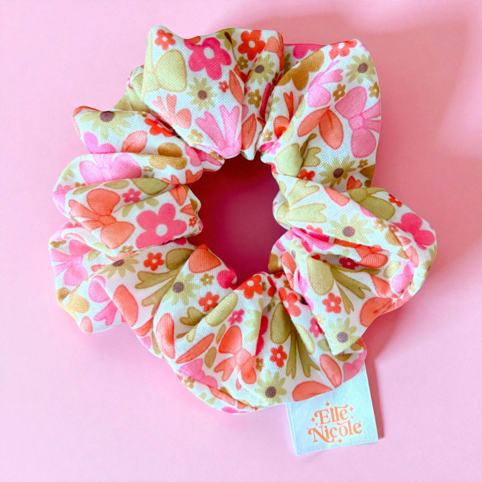 Floral patterned scrunchie with a visible brand tag on a pink background