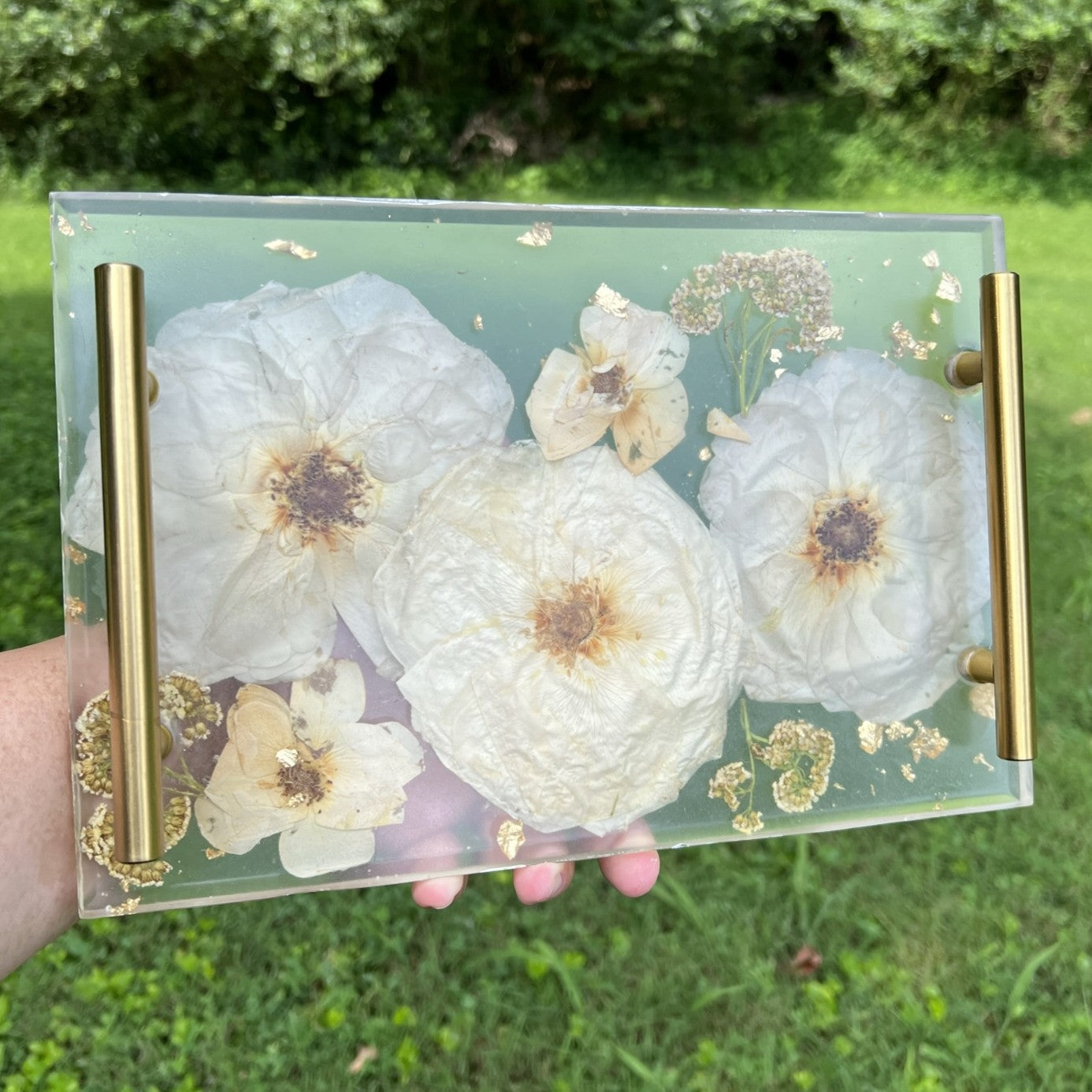 resin tray with floral design held by a hand against a grassy background