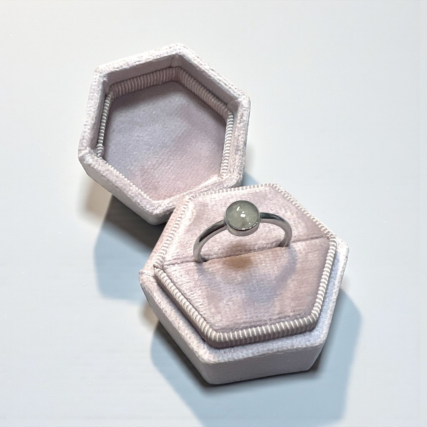 Hexagonal pink velvet jewelry box with a ring featuring a grey gemstone on a white background