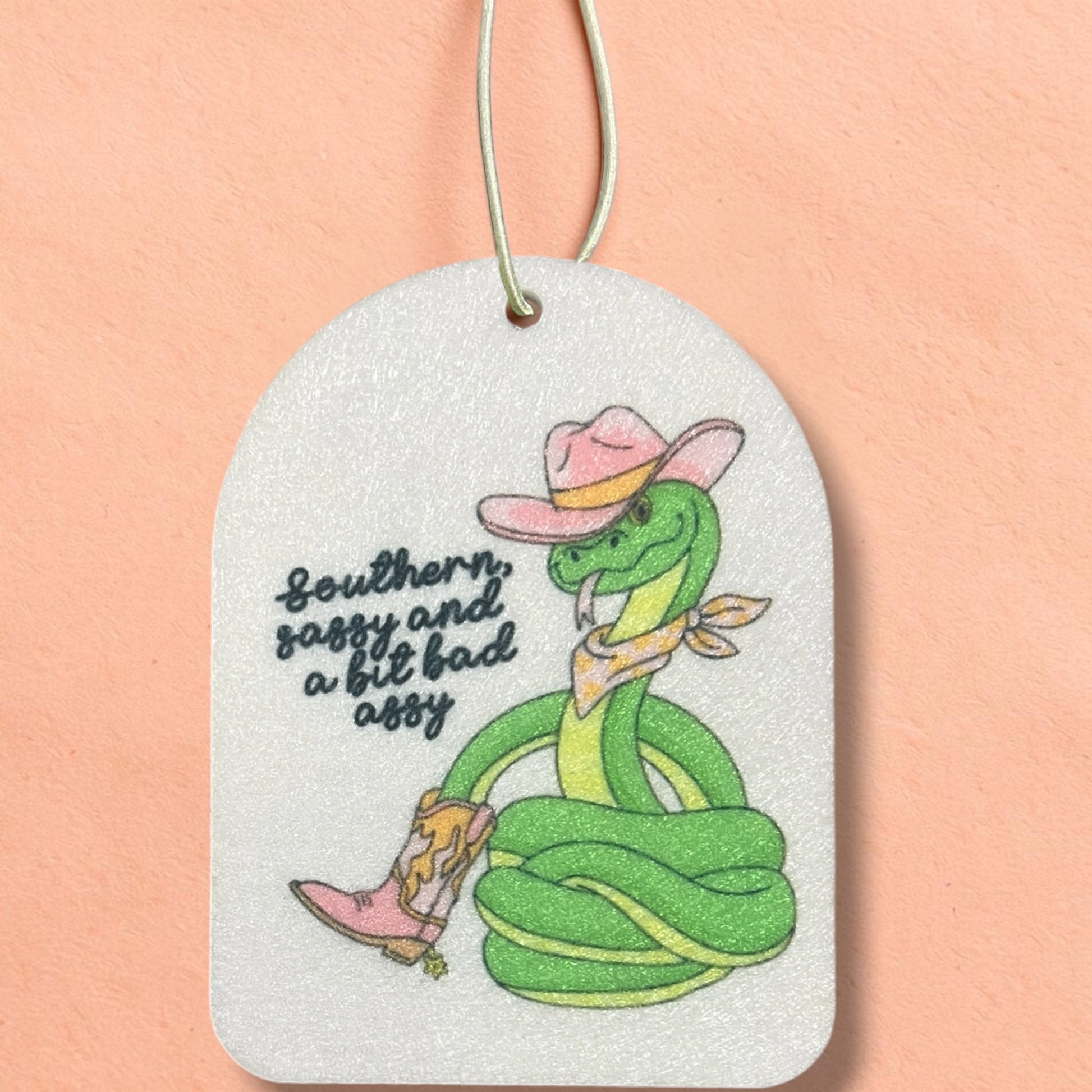 Air freshener with a cartoon snake wearing a hat and boots on a peach background