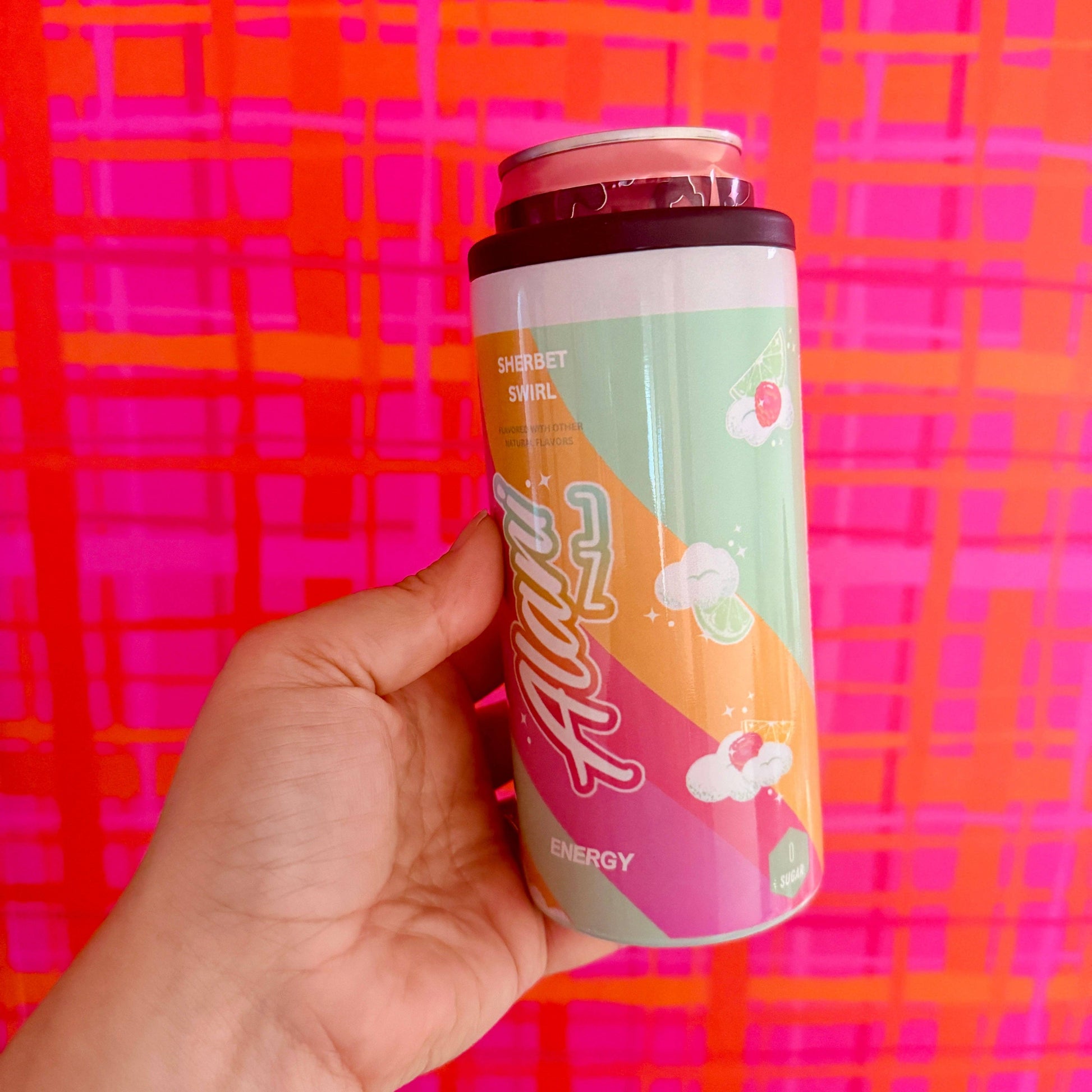 Hand holding a can of Alani Energy against a colorful patterned background