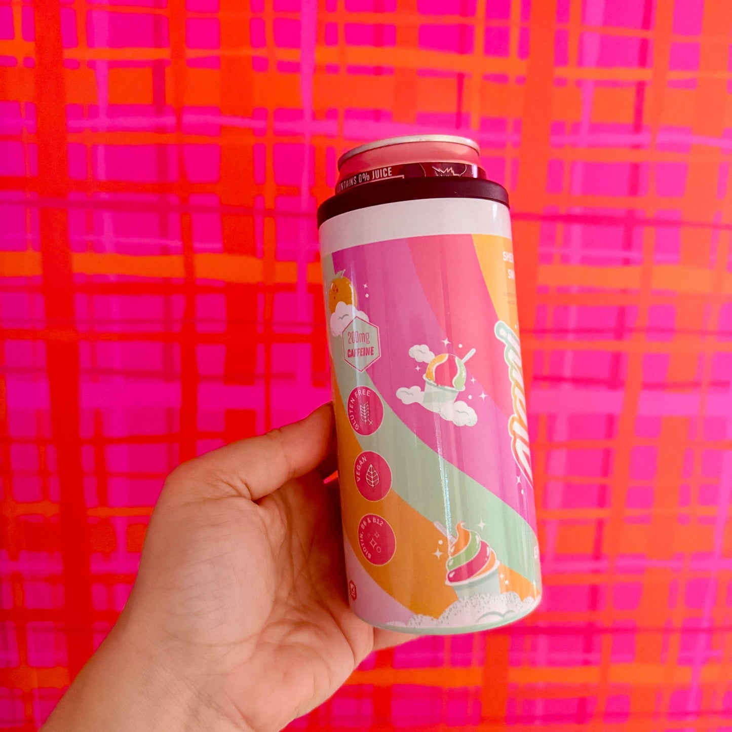 Hand holding a colorful can against a pink and orange checkered background