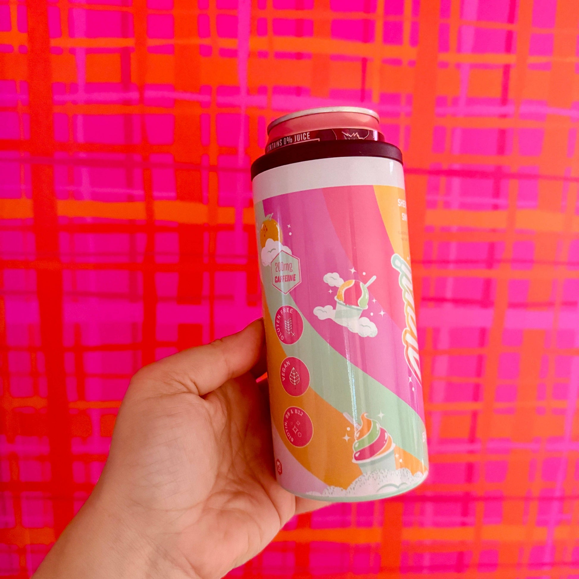 Hand holding a colorful can against a pink and orange checkered background