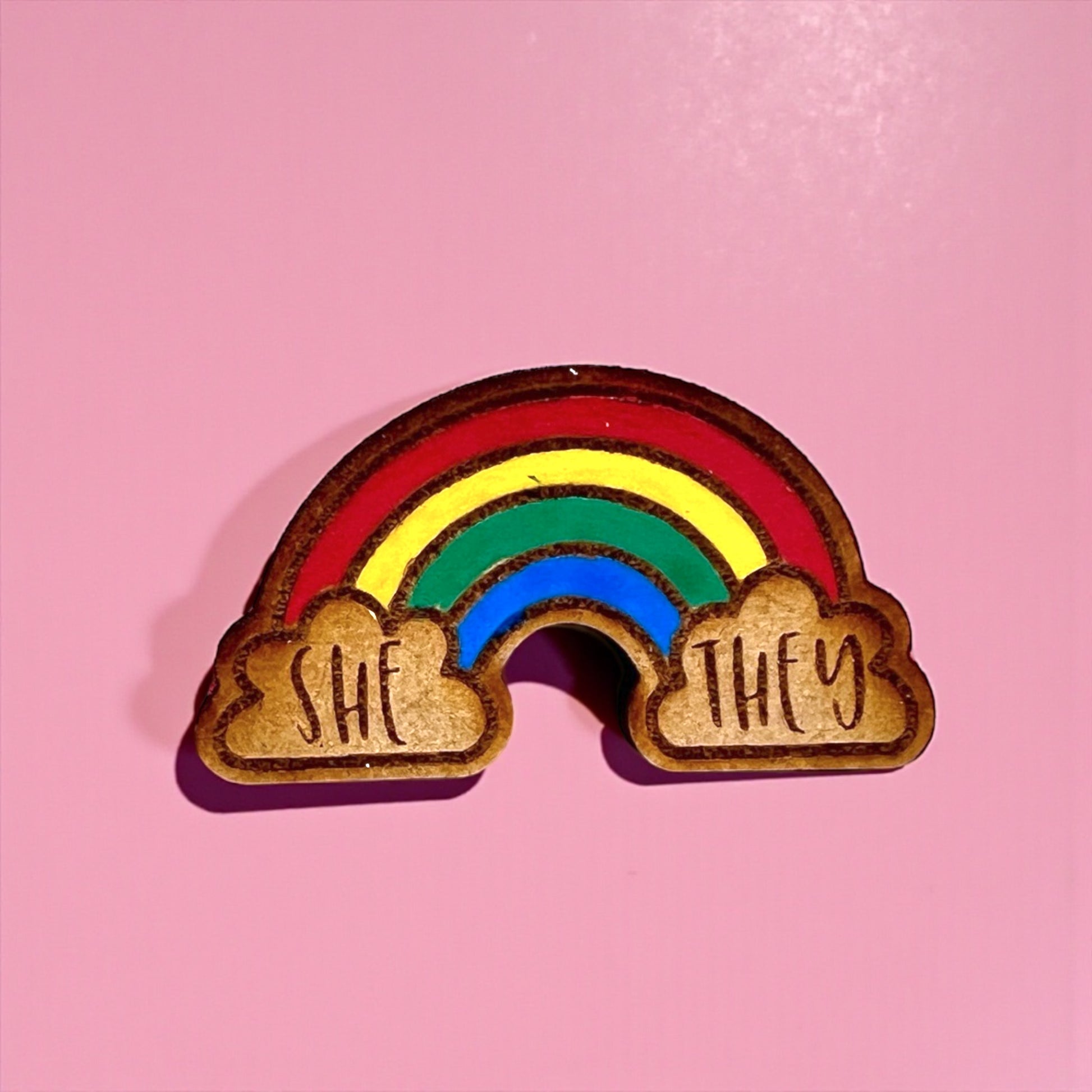 Rainbow-shaped object with 'SHE' and 'THEY' on a pink background