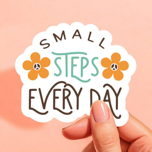 a white sticker that reads small steps every day with a yellow orange daisy on either side of the words