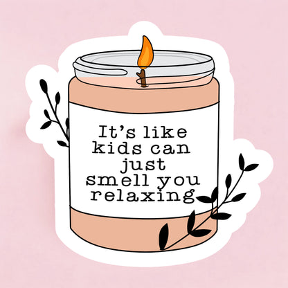 A sticker with an illustration of a candle jar and a lit candle, with the text 'It's like kids can just smell you relaxing' written on it.