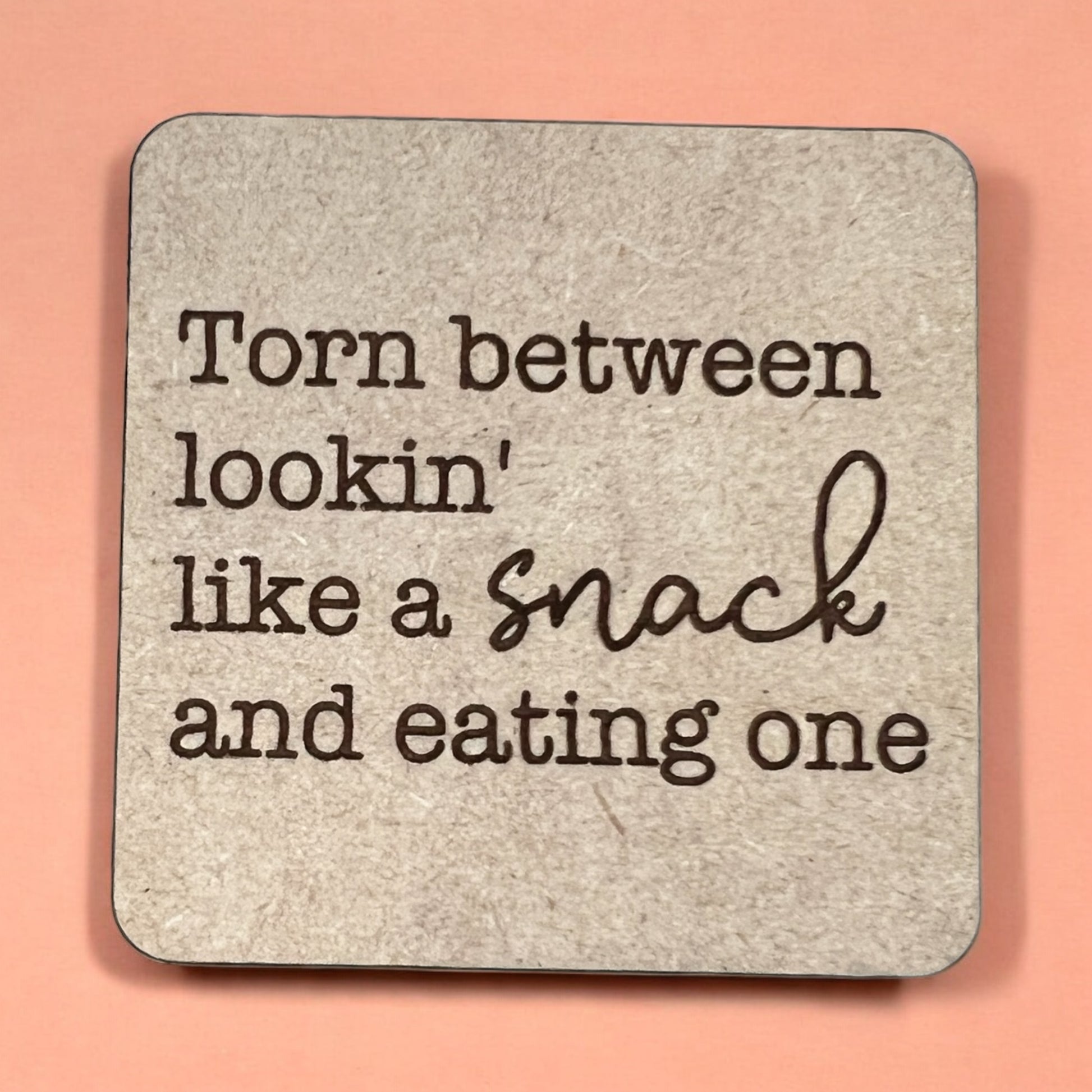 A square magnet with a humorous quote printed on it, placed against a pink background.