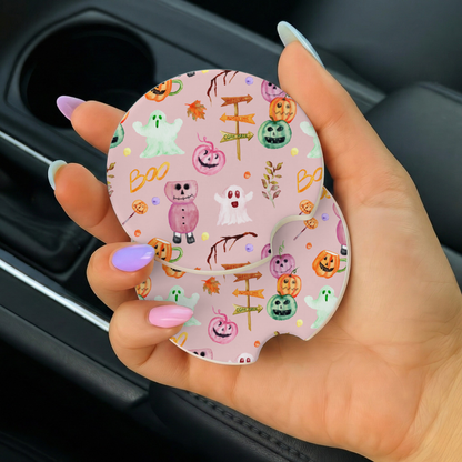 Hand holding a pink car coaster with Halloween-themed design inside a vehicle.
