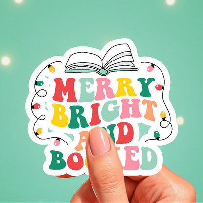 Colorful sticker with 'Merry Bright and Booked' text held against a teal background with lights.