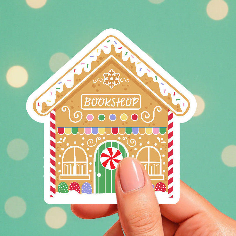 Hand holding a gingerbread house-shaped bookshop sticker against a green background with polka dots.
