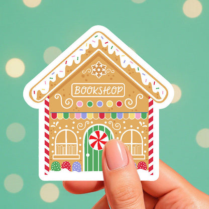 Hand holding a gingerbread house-shaped bookshop sticker against a green background with polka dots.