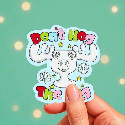Sticker with cartoon moose and text 'Don't Hog The Hog' held by a hand against a light green background.