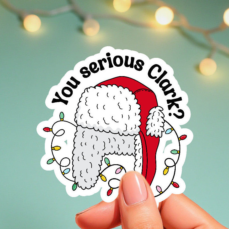 Sticker with a Christmas-themed design held by a hand against a light green background with string lights.