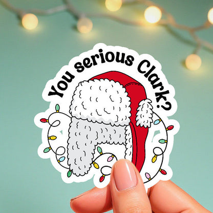 Sticker with a Christmas-themed design held by a hand against a light green background with string lights.