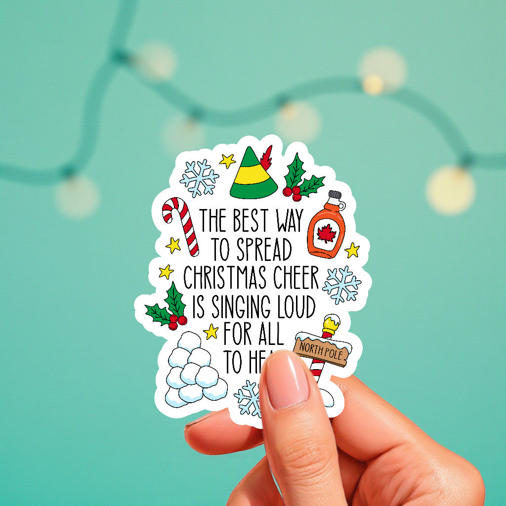 Hand holding a Christmas-themed sticker with decorative elements on a teal background.