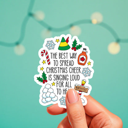 Hand holding a Christmas-themed sticker with decorative elements on a teal background.