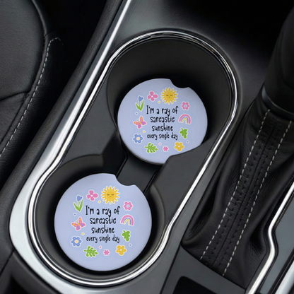Two car coasters with floral designs and text in a cup holder.