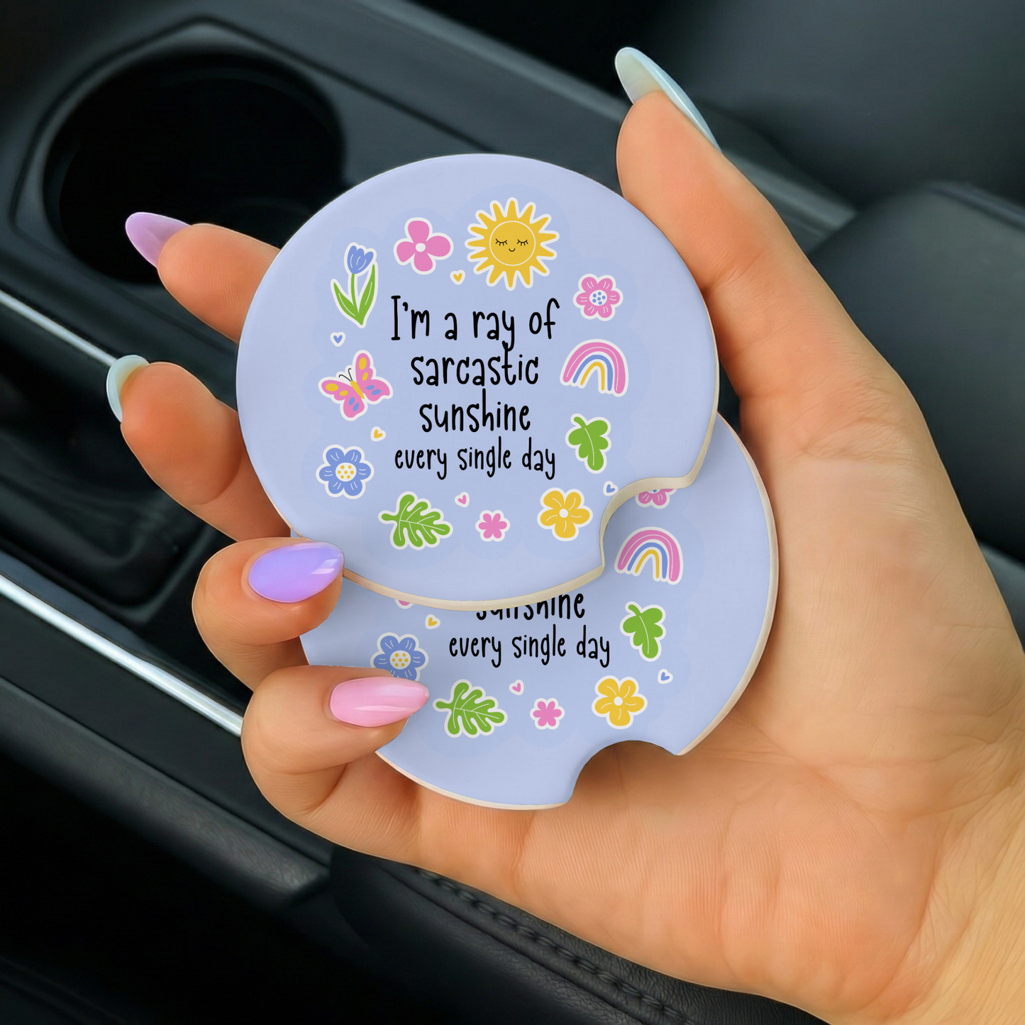 Hand holding a car coaster with colorful design and text in a car's cup holder.
