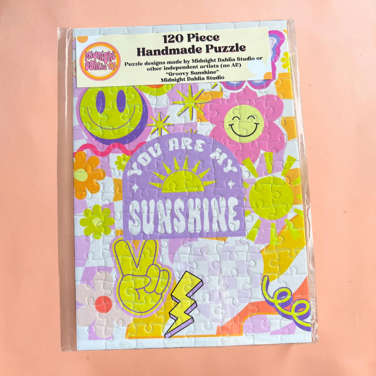 Handmade puzzle packaging with colorful designs and text on a pink background