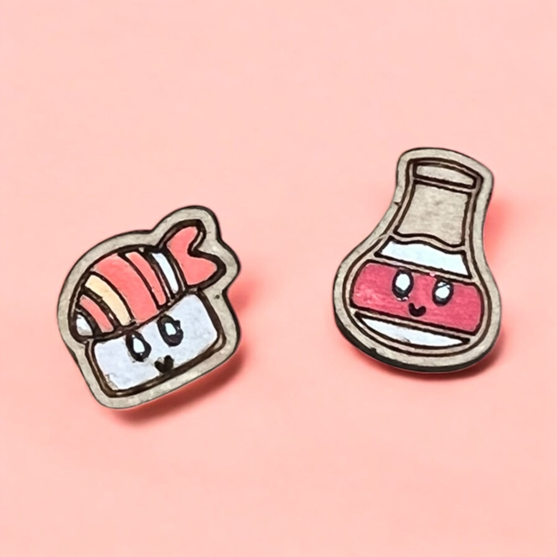 Two cartoon-style earrings, one resembling a sandwich and the other a bottle with a pink interior, on a pink background.