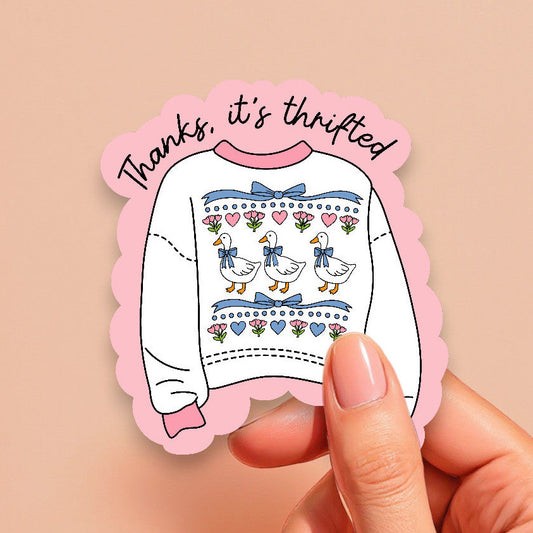 Sticker with a sweater design and text held by a hand on a beige background