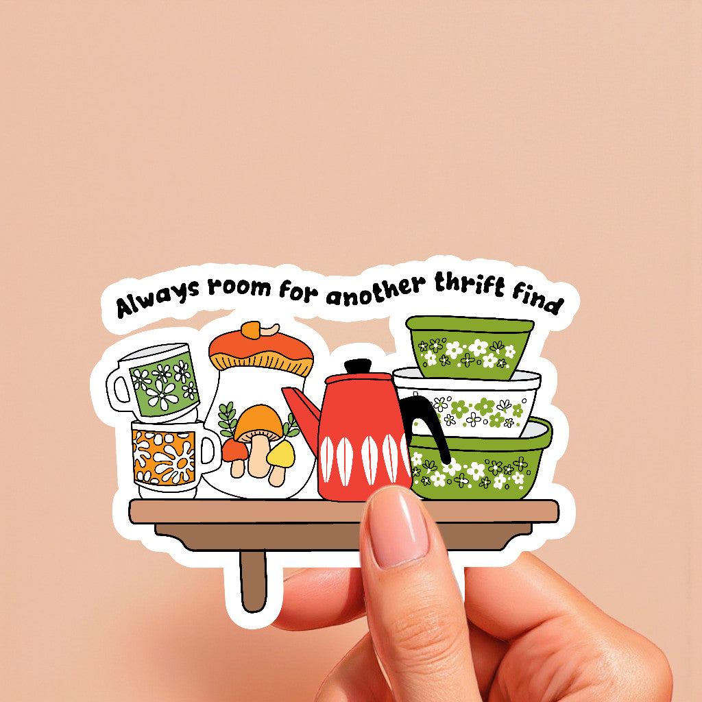 Sticker with vintage kitchen items and text 'Always room for another thrift find' held by a hand on a beige background.