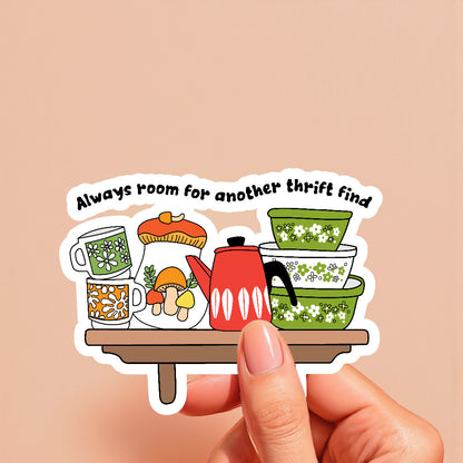 Sticker with vintage kitchen items and text 'Always room for another thrift find' held by a hand on a beige background.