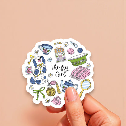 Sticker with various illustrations and the text 'Thrifty Girl' held by a hand on a beige background