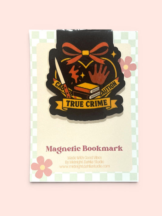 a handmade magnetic bookmark that is black with a banner that reads "true crime" on yellow with icons of a knife, books, and splatters, all surrounded by a heart with a red bow at the top.