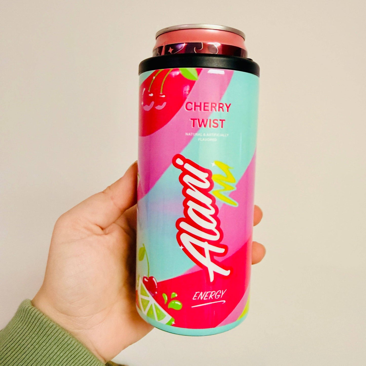 Hand holding a colorful can of Alani Nu Cherry Twist energy drink against a plain background