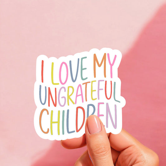 A sticker with the phrase 'I Love My Ungrateful Children' in multicolored letters, held against a pink background.