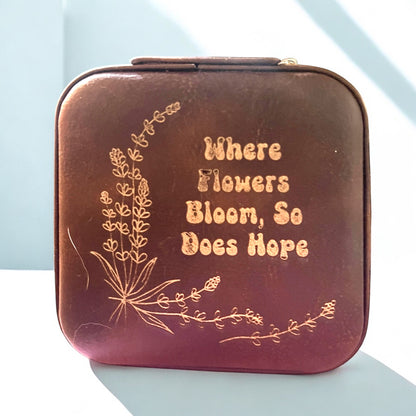 a brown jewelry box with floral accents and words engraved in gold that read 'where flowers bloom so does hope'