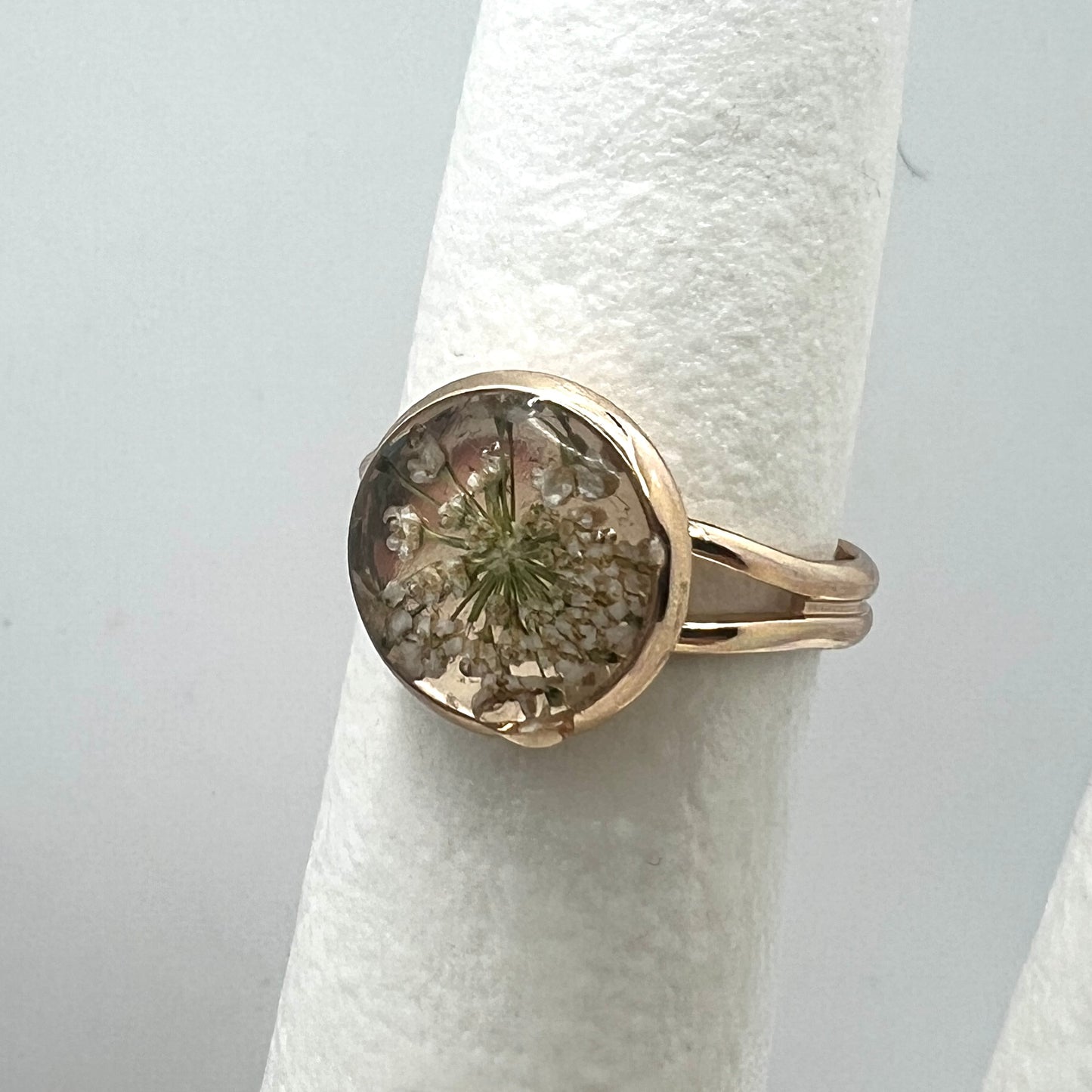 Gold ring with a circular design featuring a natural element on a white cylindrical object.