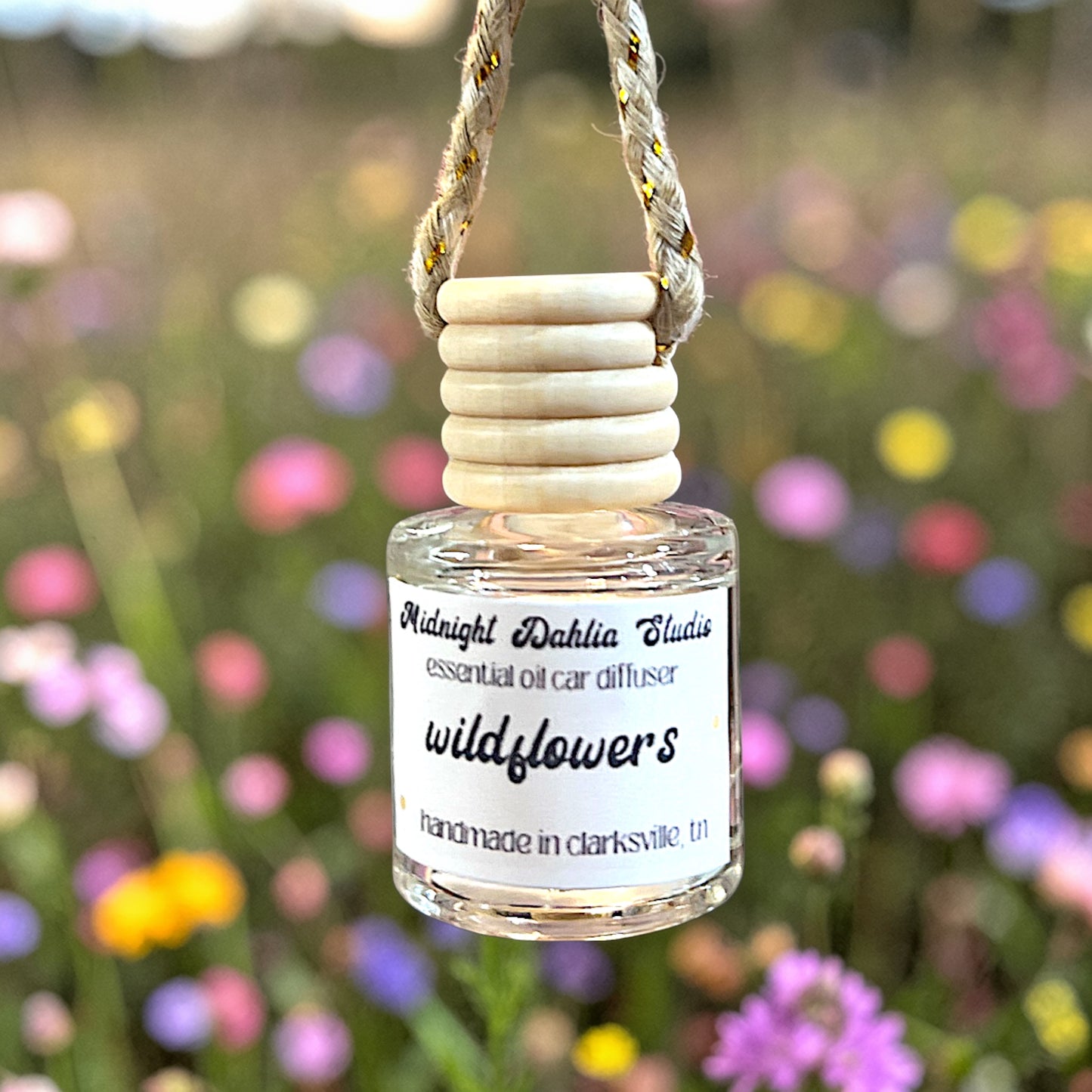 Small bottle of 'wildflowers' essential oil car diffuser with wooden top against a blurred floral background