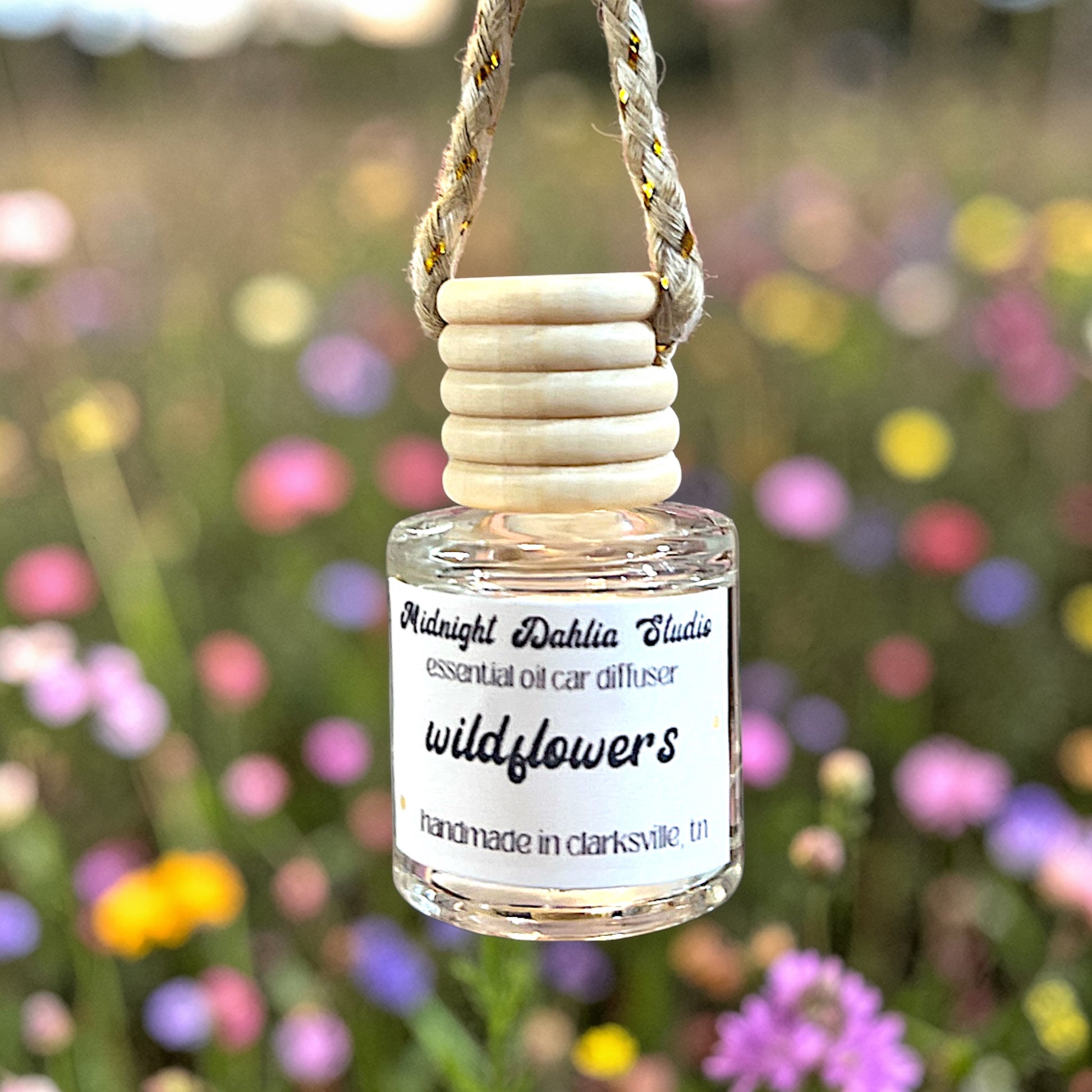 Small bottle of 'wildflowers' essential oil car diffuser with wooden top against a blurred floral background