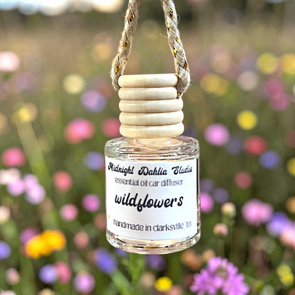 Small bottle of 'wildflowers' essential oil car diffuser with wooden top against a blurred floral background