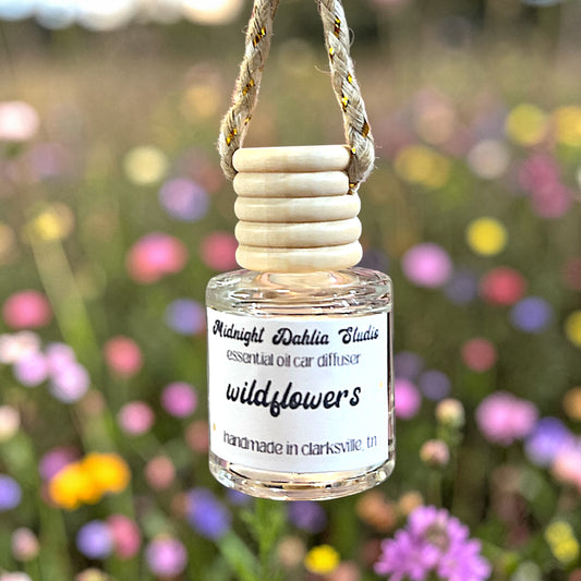 Small bottle of 'wildflowers' essential oil car diffuser with wooden top against a blurred floral background