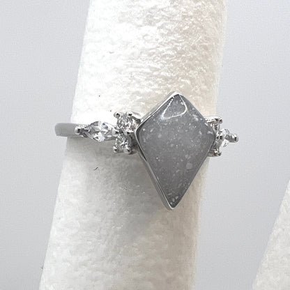 Silver ring with a gray stone on a white cylindrical stand