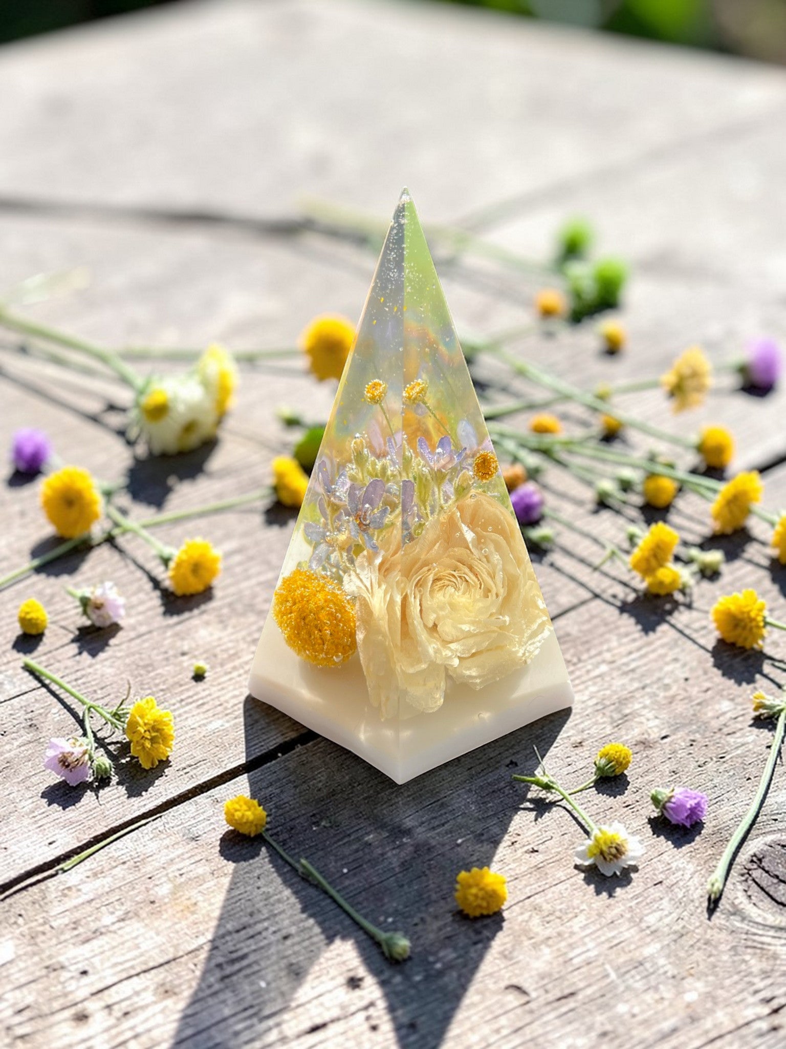 Triangular resin sculpture with flowers on a wooden surface with scattered flowers