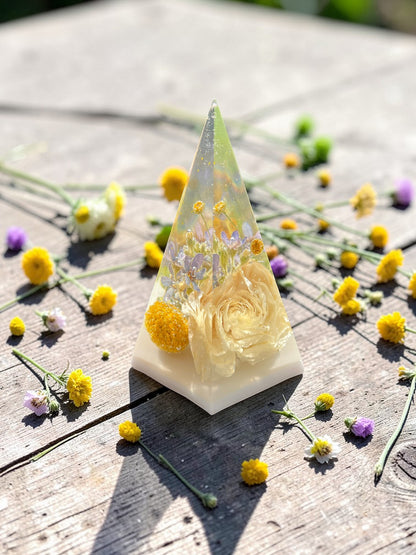 Triangular resin sculpture with flowers on a wooden surface with scattered flowers
