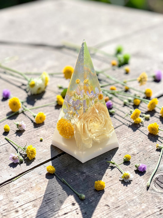 Triangular resin sculpture with flowers on a wooden surface with scattered flowers